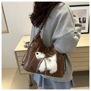 Detail einer braunen Leder-Schultertasche mit weißer Plüschpuppe und karierter Schleife