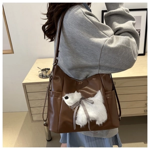 Detail der braunen Kunstleder-Schultertasche mit 3D-Plüschwelpen und einer Schleife