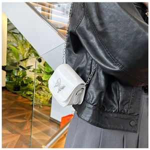 Detailed view of mini white crossbody bag with silver butterfly and metal chain