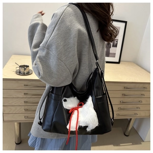Detail der schwarzen Hobo-Tasche mit weißem Plüsch-Hundeaufnäher und rotem Band