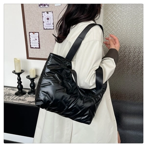 Detailed view of black quilted puffer shoulder bag with wide strap on model