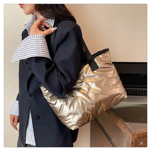 Close-up of metallic champagne quilted tote bag with black strap worn by a model