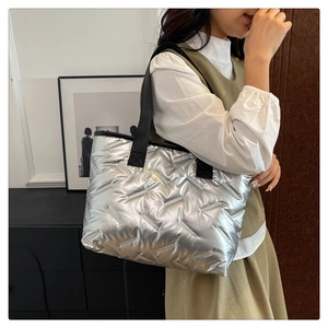 Silver quilted tote bag shown on a model for scale with black webbing handles