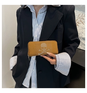 Close-up of brown suede clutch featuring a rhinestone skull motif and metal zipper