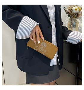 Detail of tan suede long wallet with rhinestone skull motif held by a model