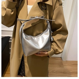 Sac hobo argenté avec poignée décorative à nœud porté par un mannequin dans un décor chaleureux