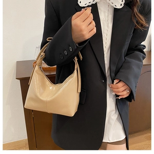 Détail d'un sac seau verni beige brillant avec poignée porté avec un blazer noir élégant