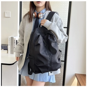 Minimalist black nylon backpack showing vertical zipper and side pocket on a model