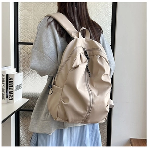 Detail of cream casual backpack with pleated design shown on a model in a school setting