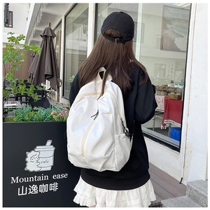 Minimalist white nylon backpack featuring diagonal front zip pocket in a cafe setting