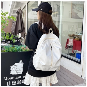 White casual nylon backpack with vertical zipper pocket shown in an outdoor cafe setting