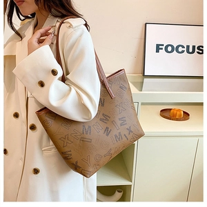 Close-up of brown leather tote bag with letter print and slim straps on a model