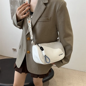 White nylon shoulder bag with wide geometric strap and woven charm on a model