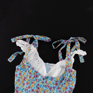 Detail van bloemenjurk met blauwe stof, gele bloemen en witte kanten afwerking