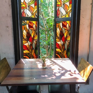 Stained glass window film with maple leaf design casting colorful light on a wooden table