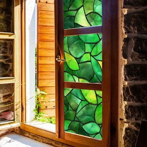 Close-up of decorative window film with green leaf pattern and stained glass texture
