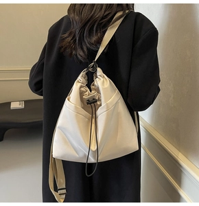 Close-up van de crèmekleurige bucket bag met verstelbare brede stoffen riem op zwarte jas