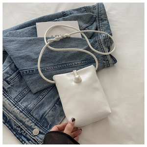 Détail d'un sac bandoulière blanc minimaliste avec un fermoir perle sur tissu denim