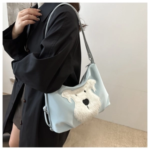 Detail of light blue shoulder bag with white plush dog patch shown on model side