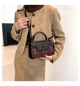 Detail of red and green plaid woolen crossbody bag with black leather strap on model