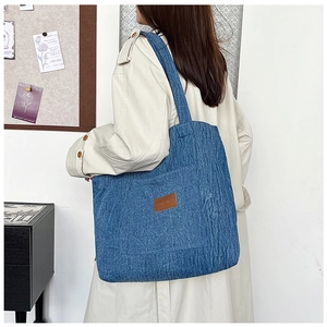 Detail of blue denim tote bag with vertical stripes and leather patch on model