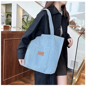 Detail of light blue denim tote bag with leather logo patch shown on female model