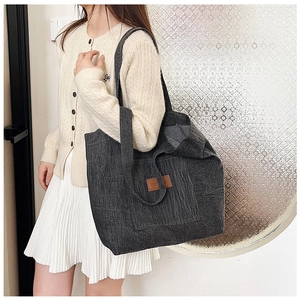 Detail of large charcoal tote bag with textured fabric and brown leather patch accent