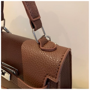 Detail of dark brown lychee leather texture and silver metal D-ring on the handbag