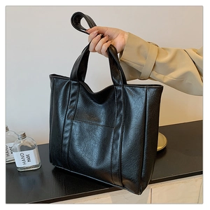 Detail view of black lychee-textured faux leather tote bag with handle and shoulder strap