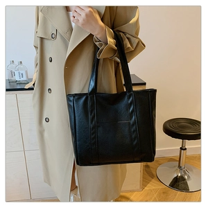 Detail of classic black leather tote bag with vertical stitching and long shoulder straps