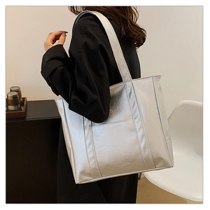 Silver metallic leather tote bag detail with wide shoulder strap on model in studio
