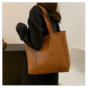 Large brown leather tote bag detail showing high-capacity design and wide shoulder straps