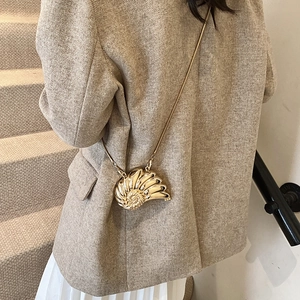 Metallic conch shell mini bag with gold chain strap shown on a model in a luxury indoor setting