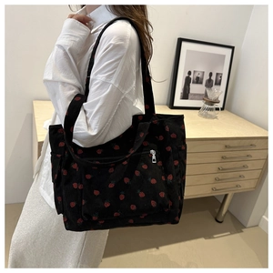 Close-up of black corduroy tote bag with red strawberry prints and functional front pocket