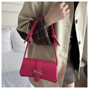 Detail of fuchsia crossbody bag with knotted strap and gold buckle on model