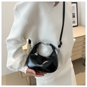 Close-up of black patent leather crescent bag with silver clover charm and logo detail