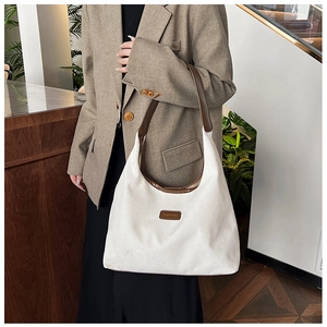 Detail of white corduroy tote bag featuring brown leather straps and square logo patch