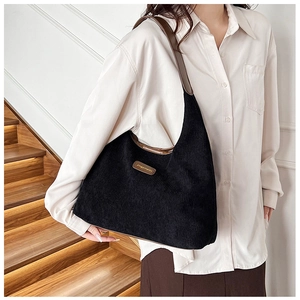 Close-up of black corduroy shoulder bag with brown leather trim and brand logo patch