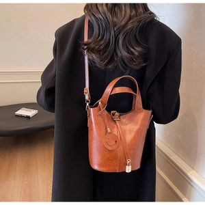 Dettaglio di una borsa a secchiello in pelle marrone con lucchetto dorato e charm