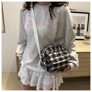 Detail view of a black and white checkered canvas crossbody bag with adjustable white strap