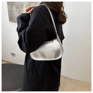 Silver metallic underarm bag with pleated texture worn on the shoulder over a black coat