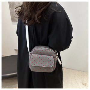 Detailed shot of a grey crossbody bag with red hearts and adjustable white strap