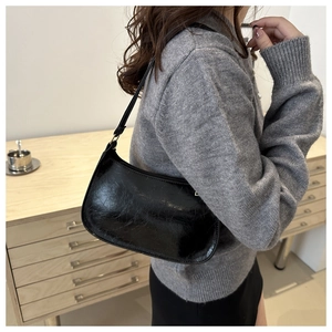 Détail d'un sac sous le bras noir brillant à texture froissée porté par un mannequin