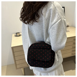 Détail d'un sac bandoulière en toile noire à motifs cœurs rouges porté par le mannequin