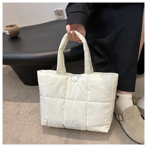 Detail of quilted off-white tote bag showing padded nylon fabric and snap closure