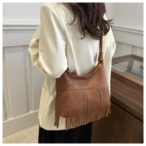 Close-up of brown litchi texture shoulder bag featuring long fringe tassels on model