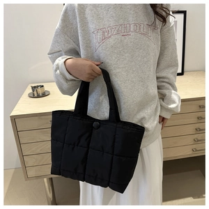 Détail d'un sac cabas matelassé noir avec coutures carrées et bouton pression sur modèle