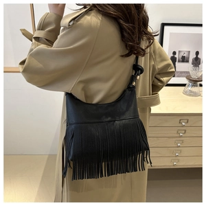 Detail of black hobo bag with long tassels and litchi grain texture on trench coat