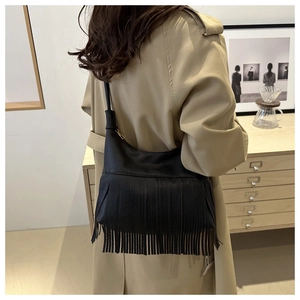 Detail of black hobo bag with long tassels and gold zipper on khaki trench coat