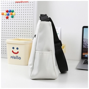 Detail of white nylon tote bag side pocket and black adjustable fabric strap on desk